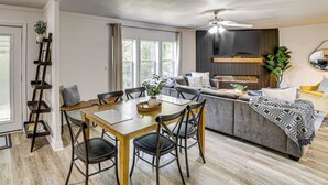 A modern living room with a dining area, a sofa, a TV, and a fireplace. - Fire Pit & Stunning Lake Views: Shell Knob Home! (Shell Knob)