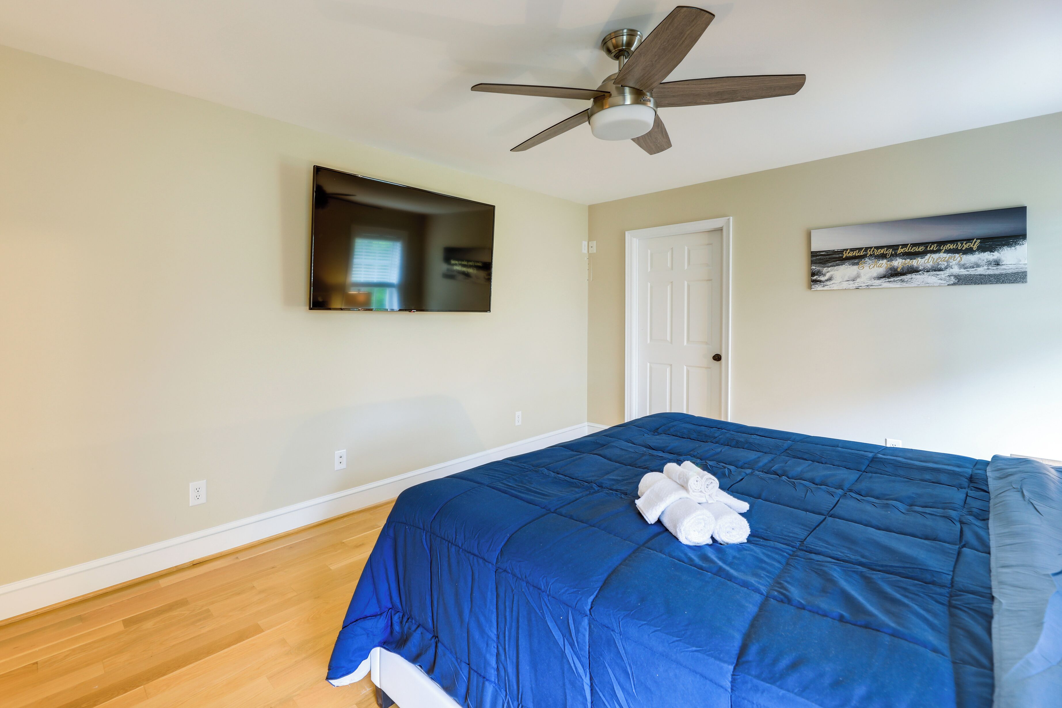 A bedroom with a bed, a ceiling fan, a door, and a wall-mounted mirror.
