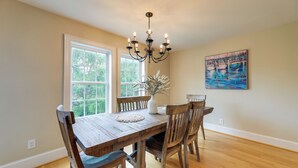 Une salle à manger avec une table et des chaises en bois, un lustre, un vase avec des plantes et un tableau au mur.