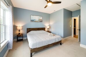 A bedroom with a large bed, two bedside tables with lamps, a ceiling fan, and a painting on the wall.