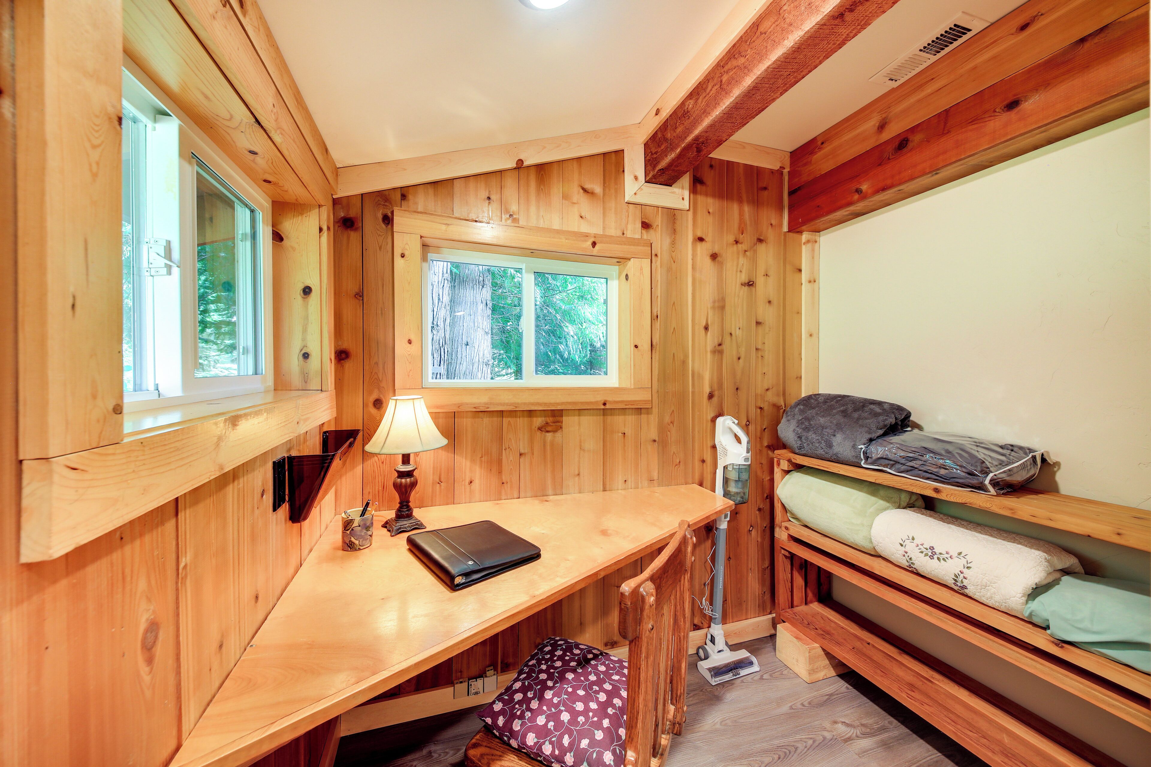 Une chambre rustique en bois avec un lit superposé, un bureau avec une lampe et une fenêtre donnant sur les arbres.