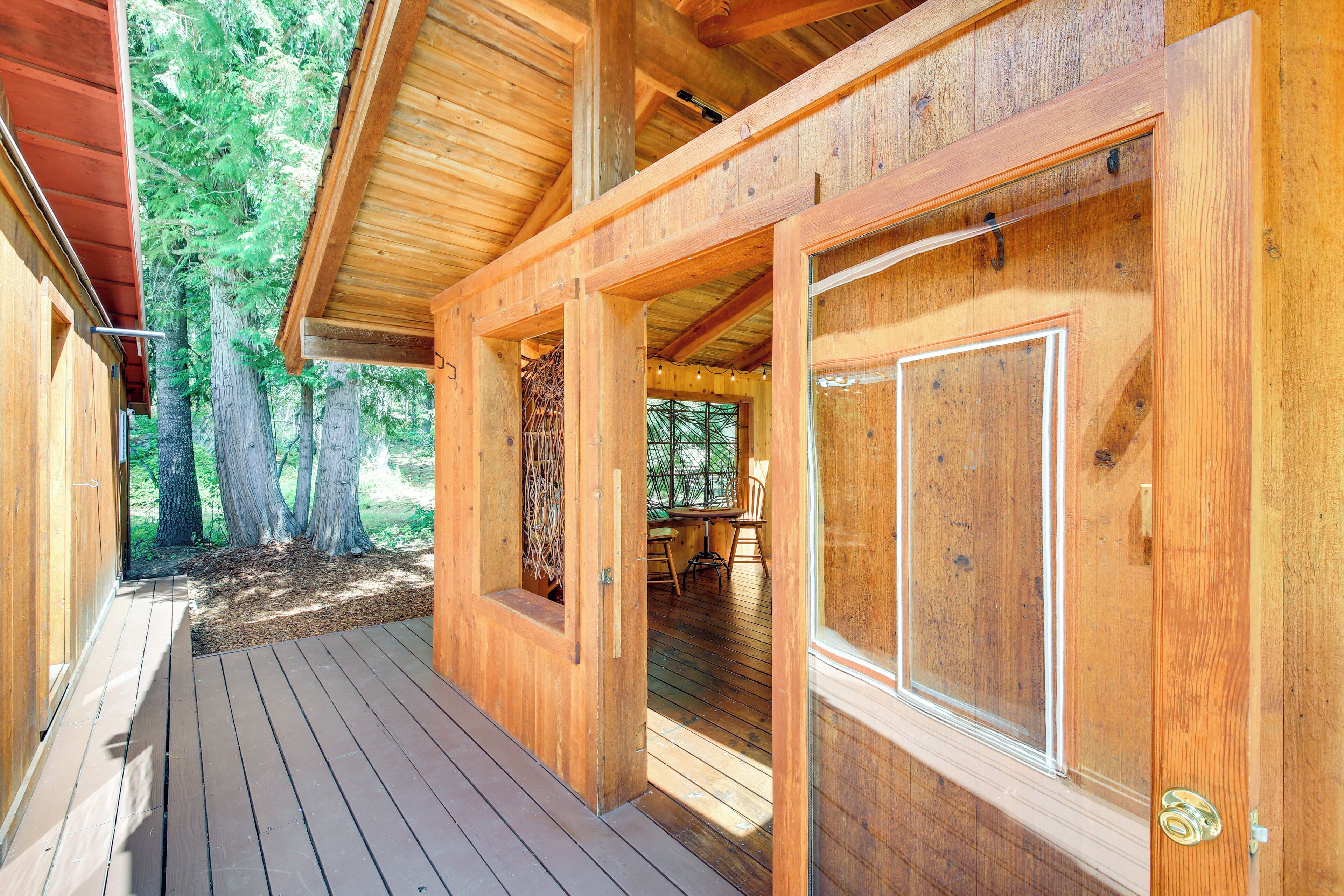 A wooden cabin with a deck, large windows, and a view of the forest.