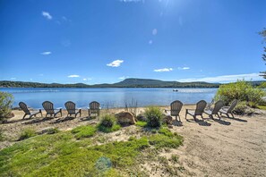 A lakeside view with chairs and tables arranged for outdoor dining, overlooking a calm lake and distant hills. - Beach & Kayaks: Waterfront Cabin on Lake Pleasant! (Speculator)