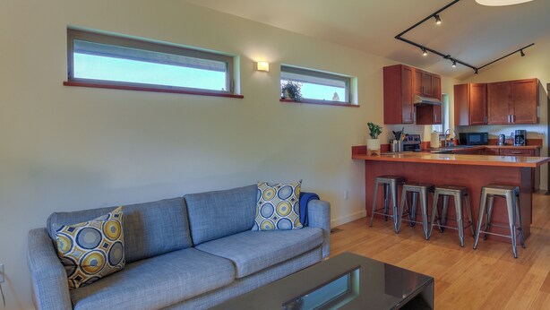 A living room with a sofa, a coffee table, and a kitchen area with a counter and stools.