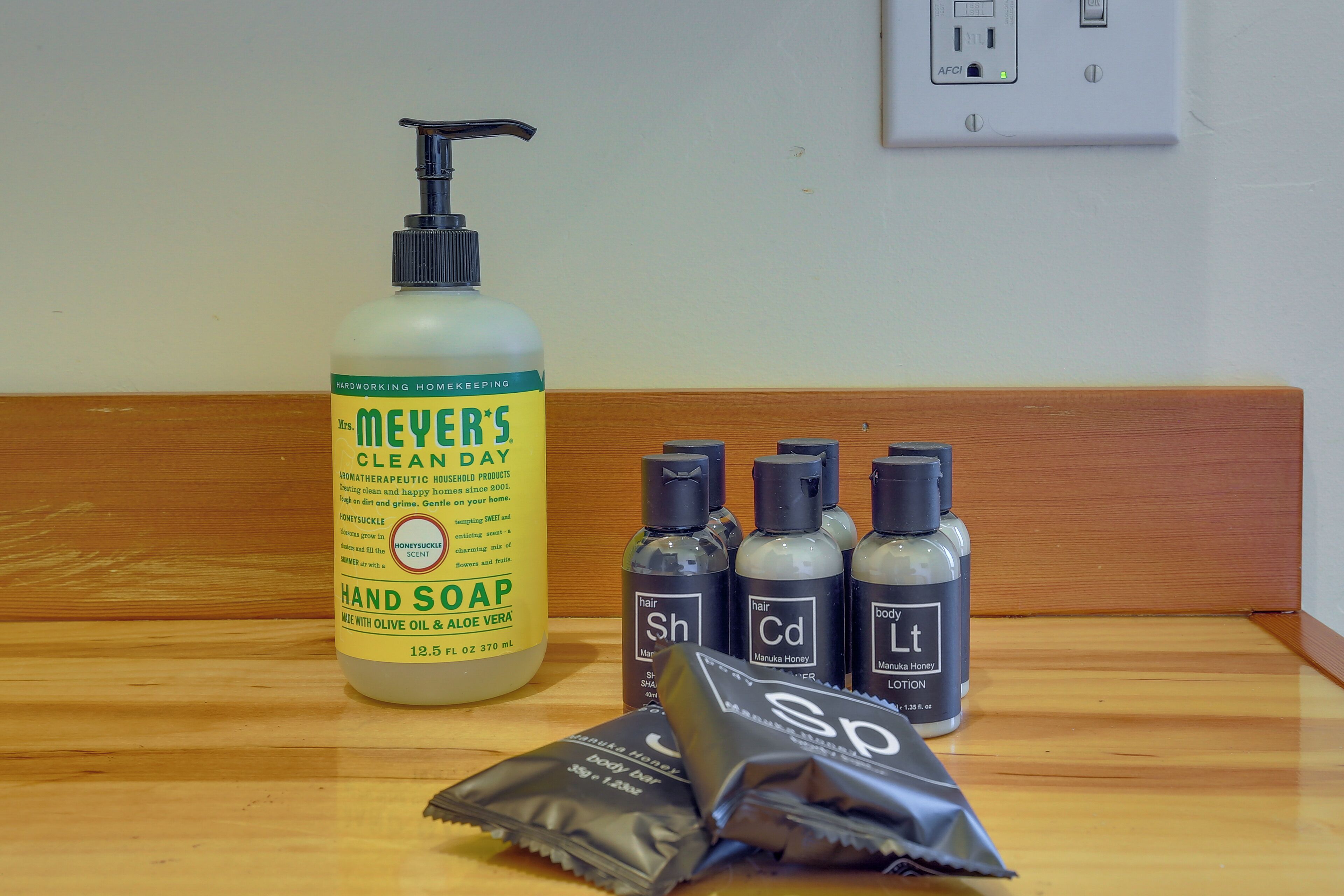 A bathroom with a wooden bench, a bottle of hand soap, and three bottles of hair care products.