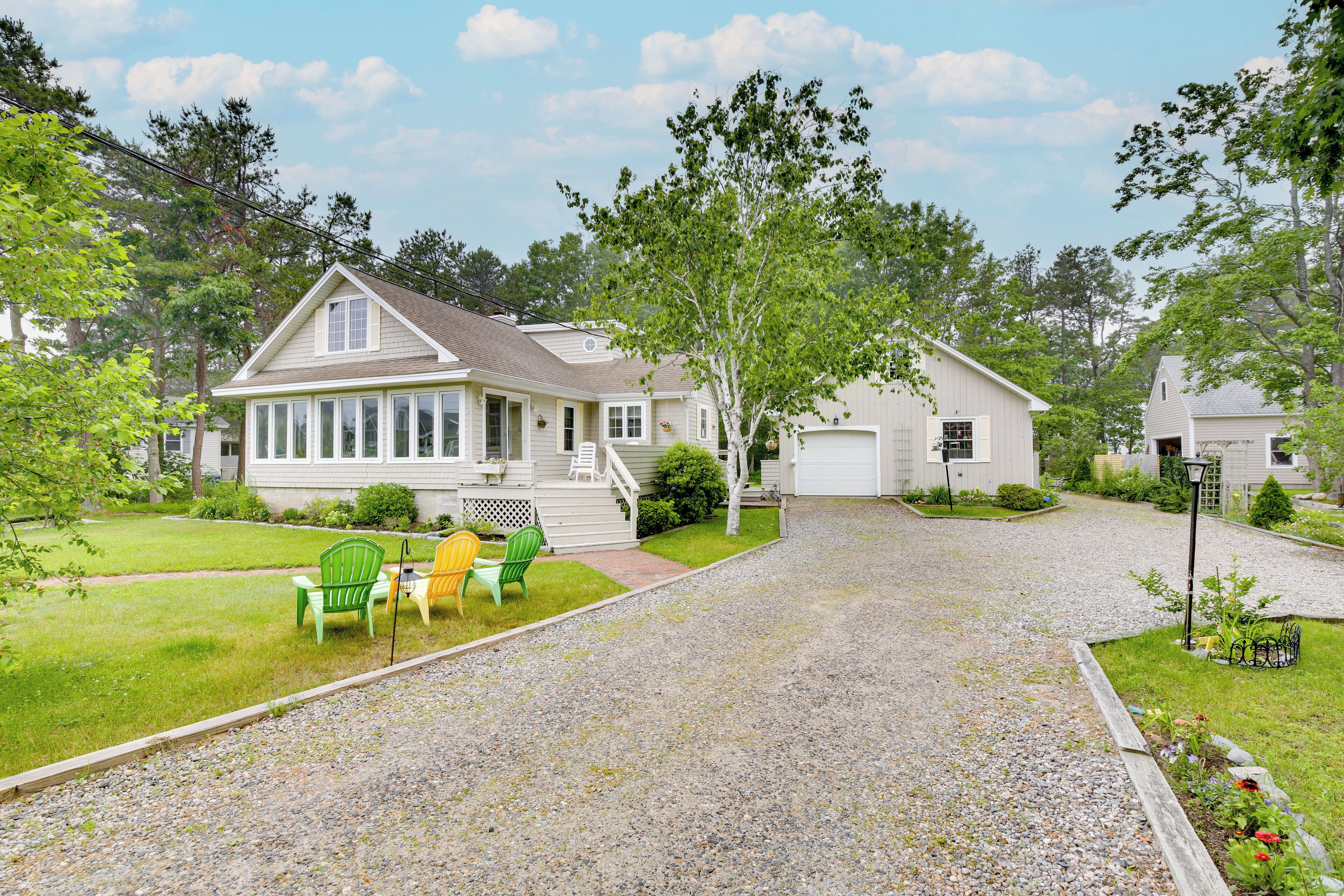 A residential area with houses, a gravel driveway, and green chairs in the yard.