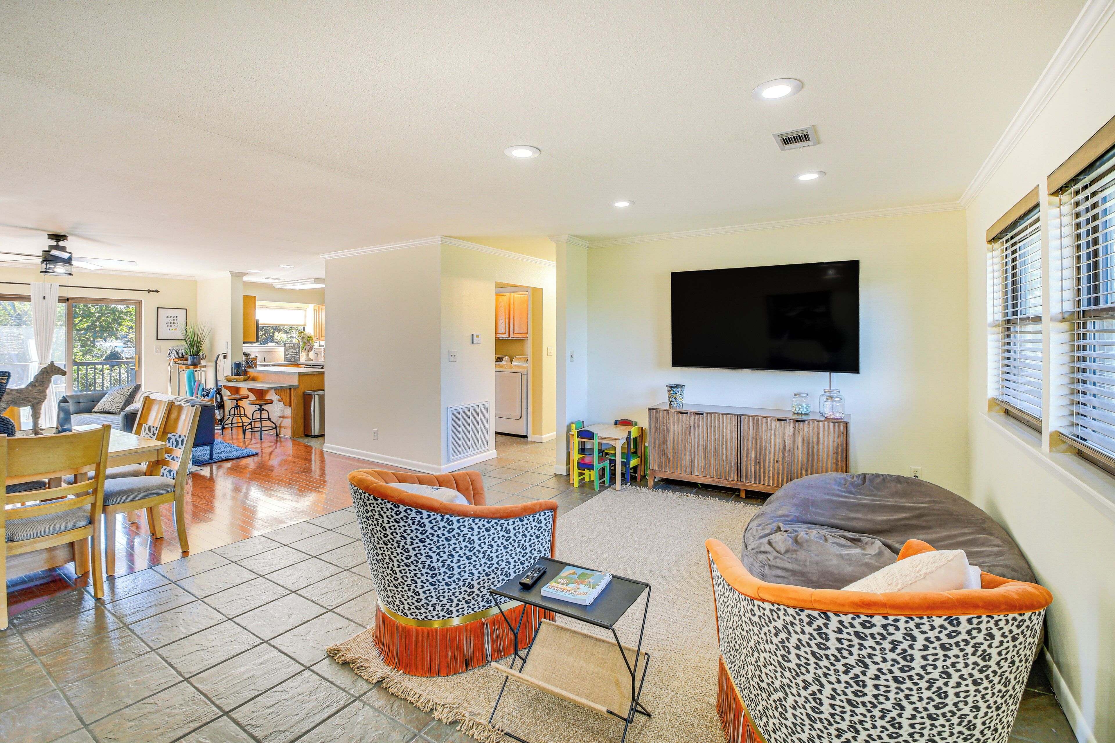 A spacious living area with a dining table, two sofas, a TV mounted on the wall, and a kitchen in the background.
