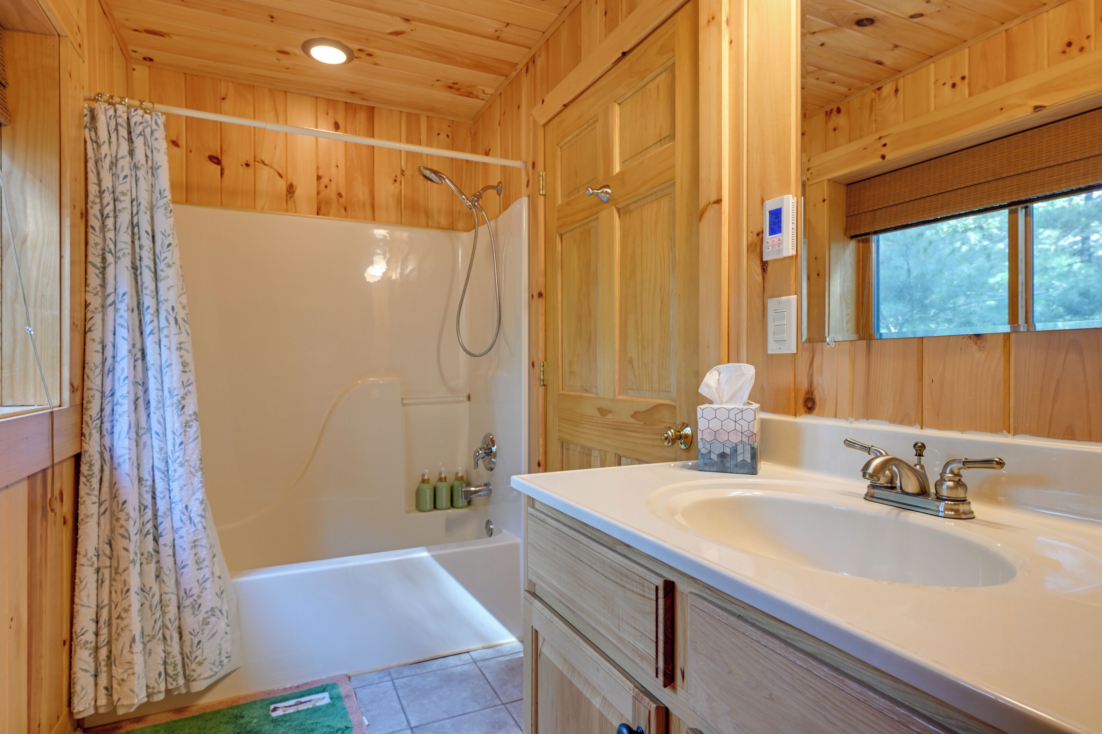 Baño de una cabaña de madera con bañera, ducha y lavamanos con espejo.