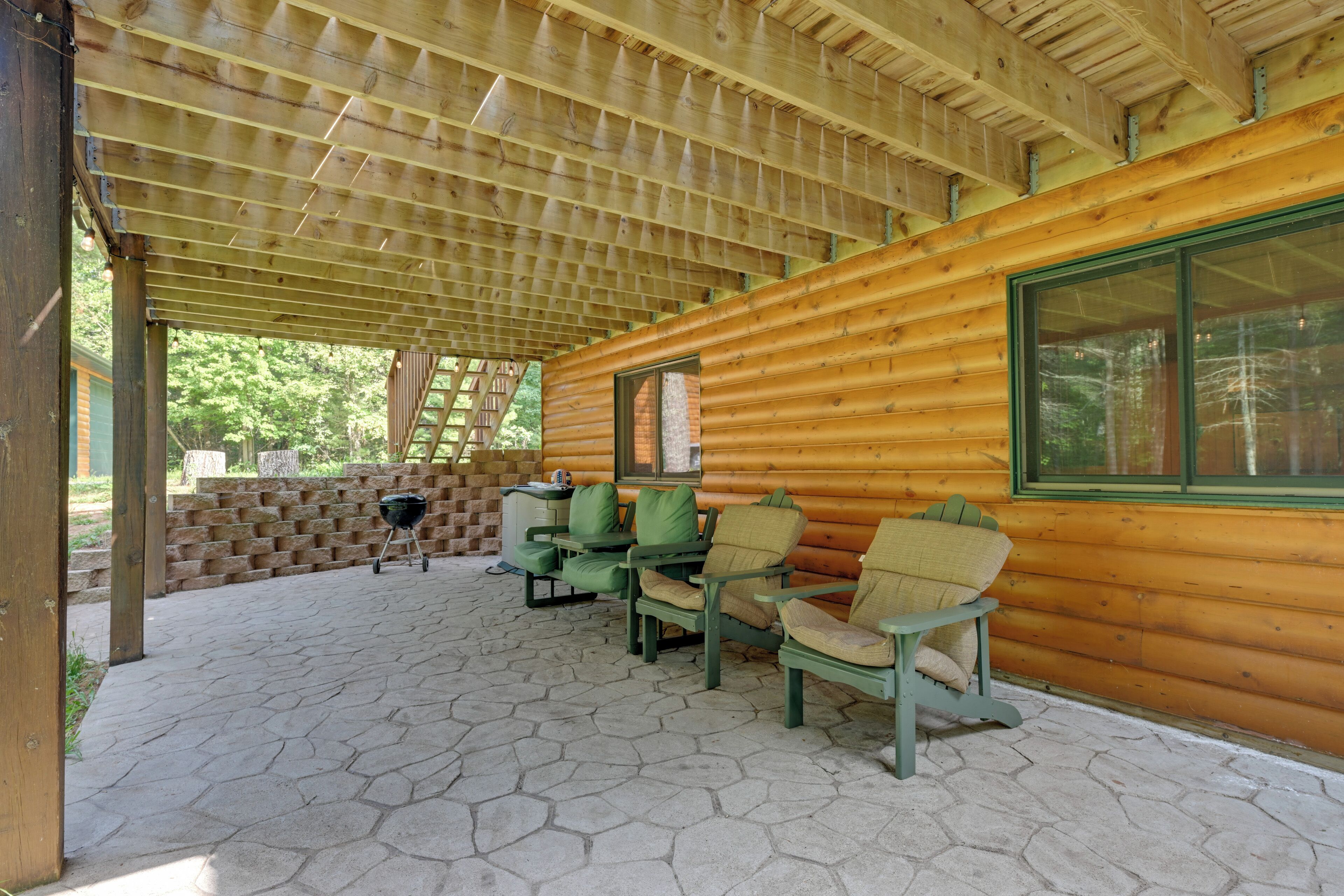 Une terrasse couverte avec un sol en pierre hexagonale, des murs en bois brut et des chaises recouvertes d’un tissu vert.