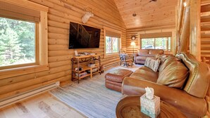 Interior de una cabaña de troncos con un sofá de cuero, estanterías de madera, un televisor y un ventilador de techo.