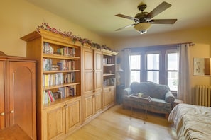 Una habitación con una estantería de madera, un ventilador de techo, un sofá y una cama.