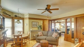 A spacious living room with a wooden floor, a round coffee table, a sofa, and a ceiling fan. - Algoma Victorian - Steps to Lake Michigan! (Algoma)