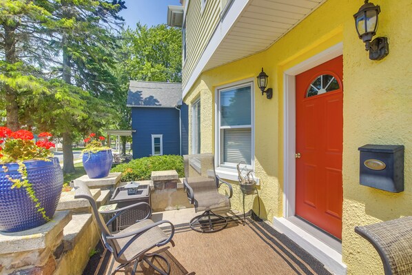 A yellow house with a red door, outdoor seating, and potted plants.