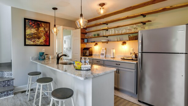 Una cocina moderna con una isla central, taburetes de bar, electrodomésticos de acero inoxidable y un cuadro decorativo.