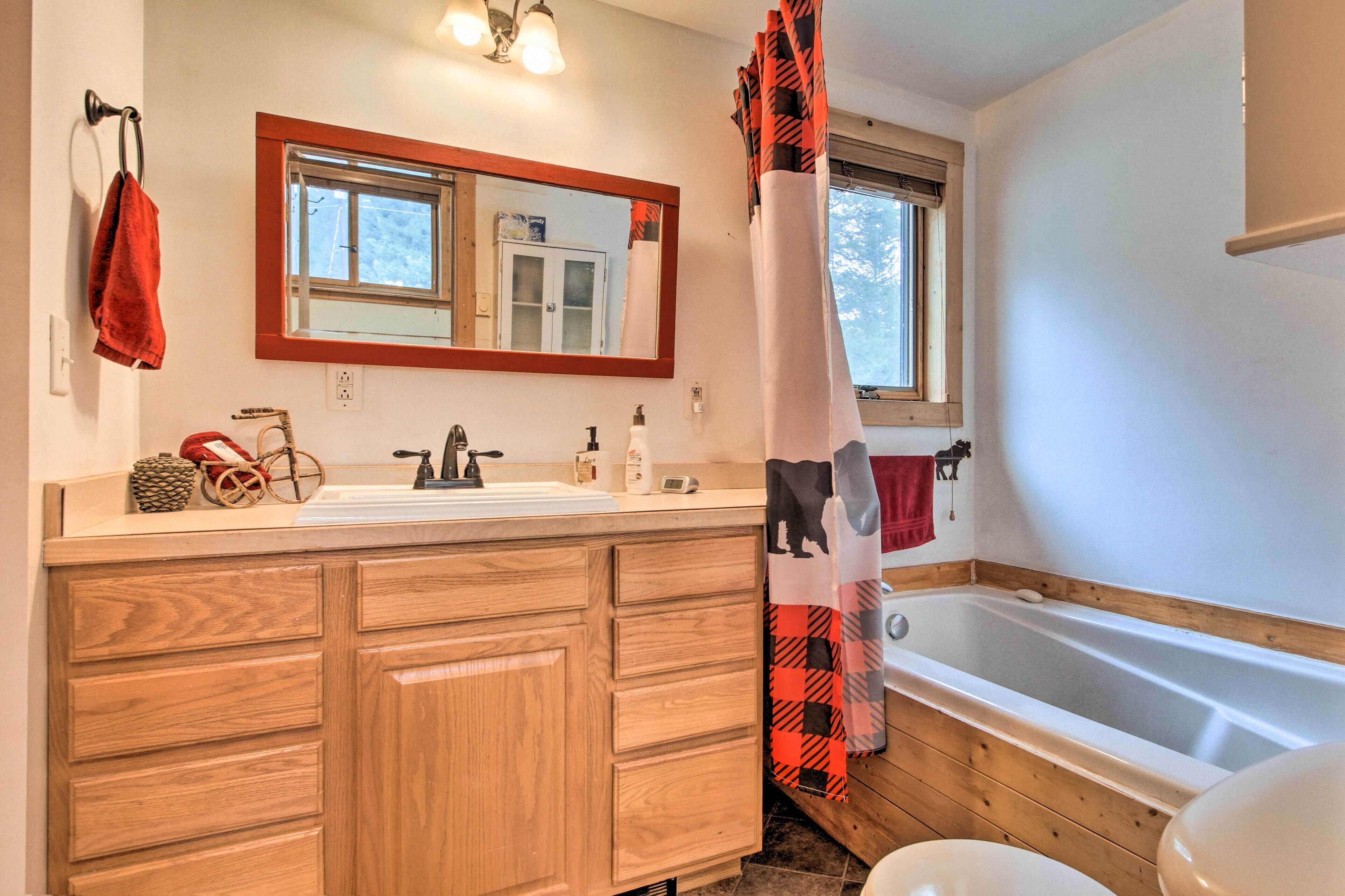 A bathroom with wooden cabinets, a sink, a mirror, a window, and a bathtub.