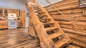 Une cuisine rustique avec des meubles en bois et un grand escalier en bois adossé à un mur fait de rondins.