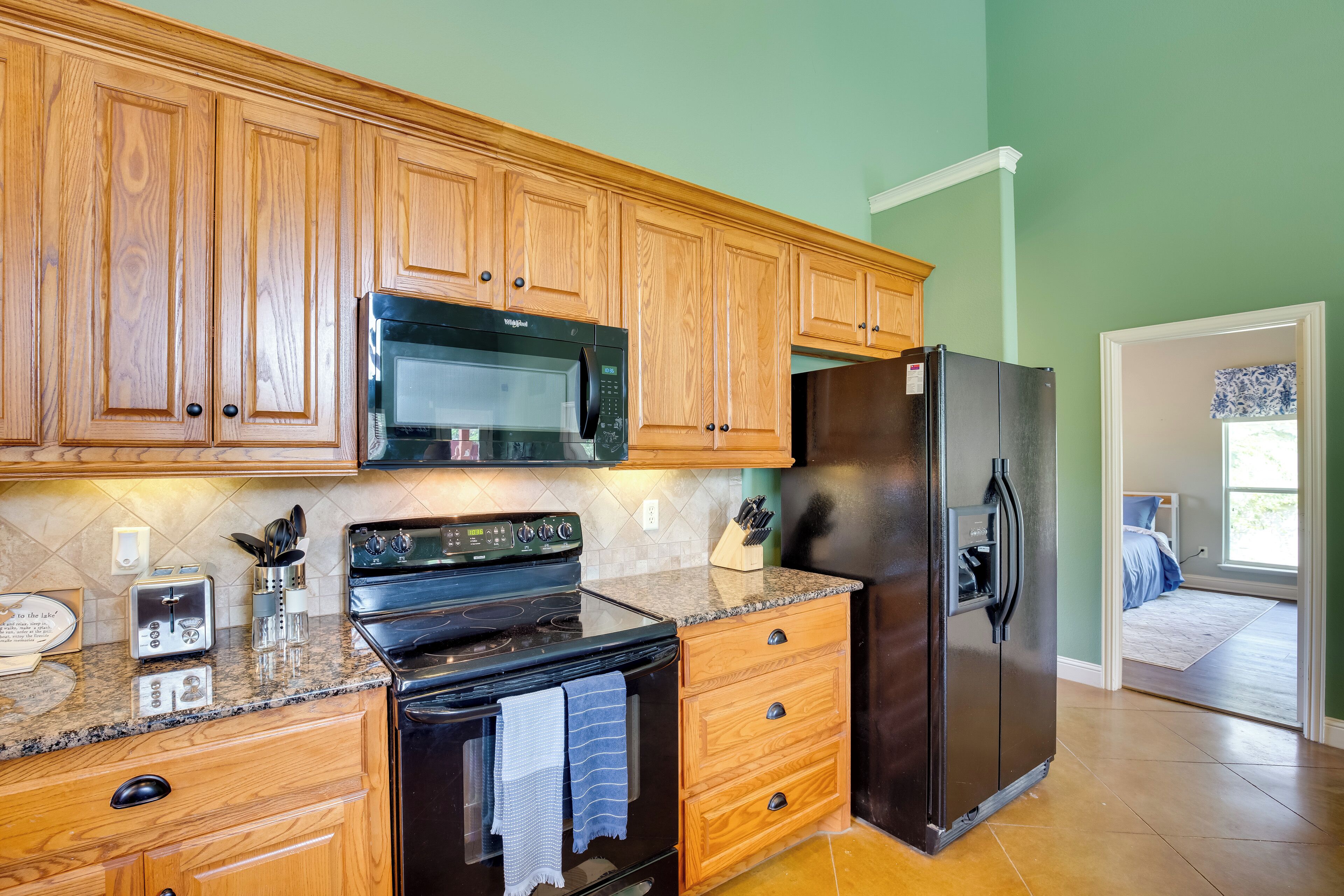 A kitchen with wooden cabinets, a black microwave, a stove, and a refrigerator.