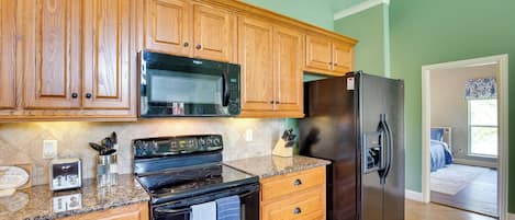 A kitchen with wooden cabinets, a black microwave, a stove, and a refrigerator.