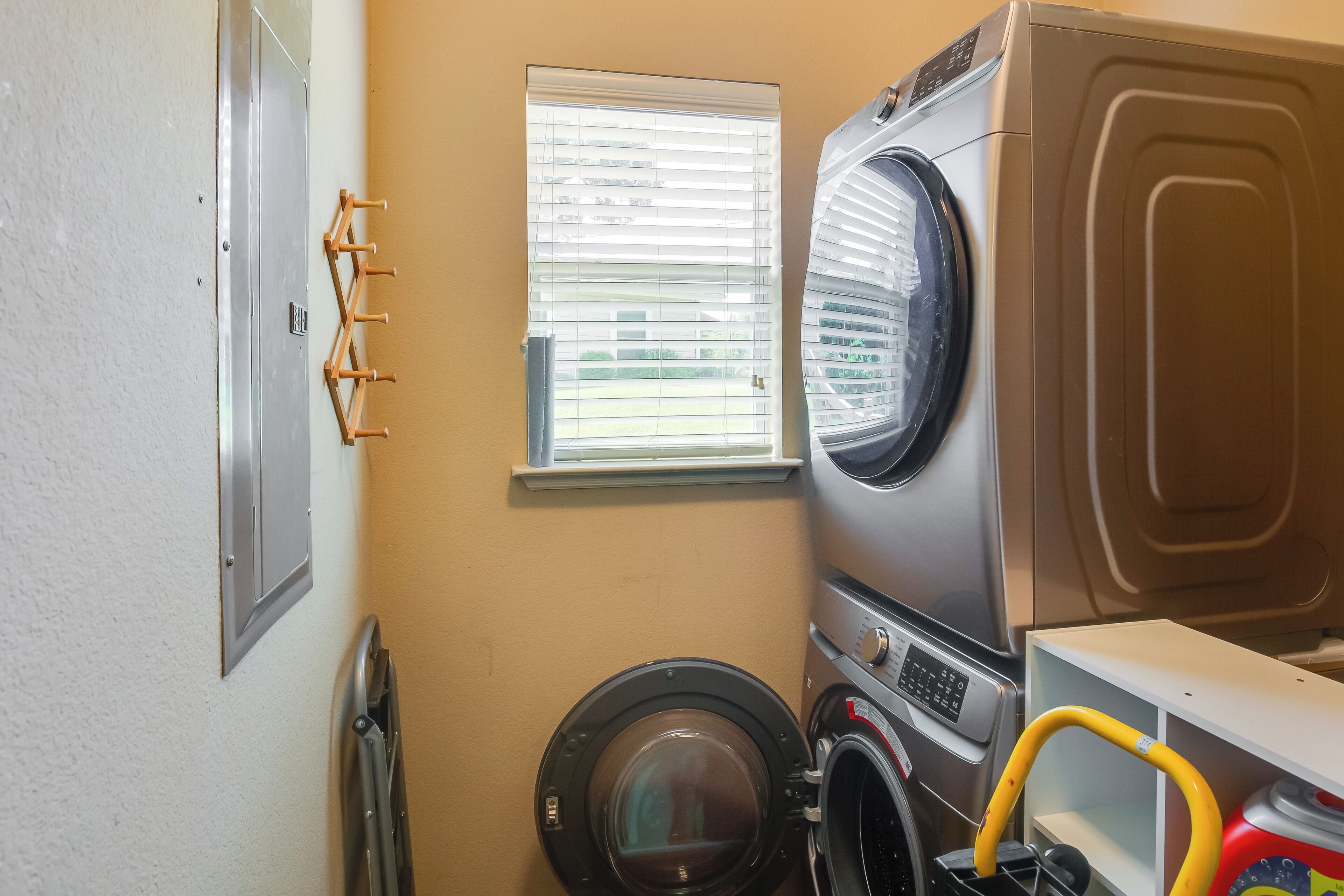 A compact laundry room with a front-loading washer and dryer, a window with blinds, and a metal rack for hanging clothes.