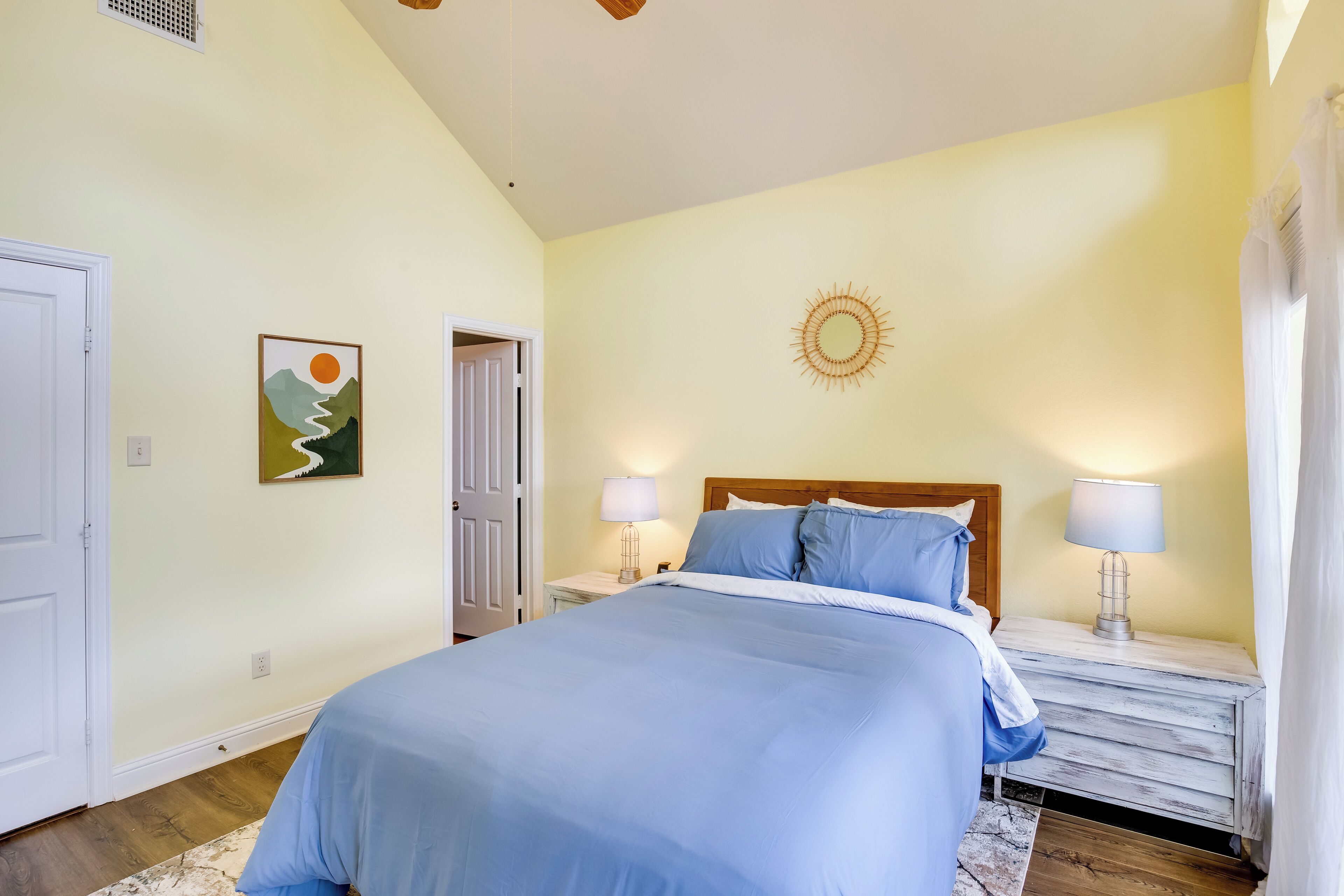 Un dormitorio con cama, dos mesitas de noche con lámparas, una puerta y un adorno en la pared.
