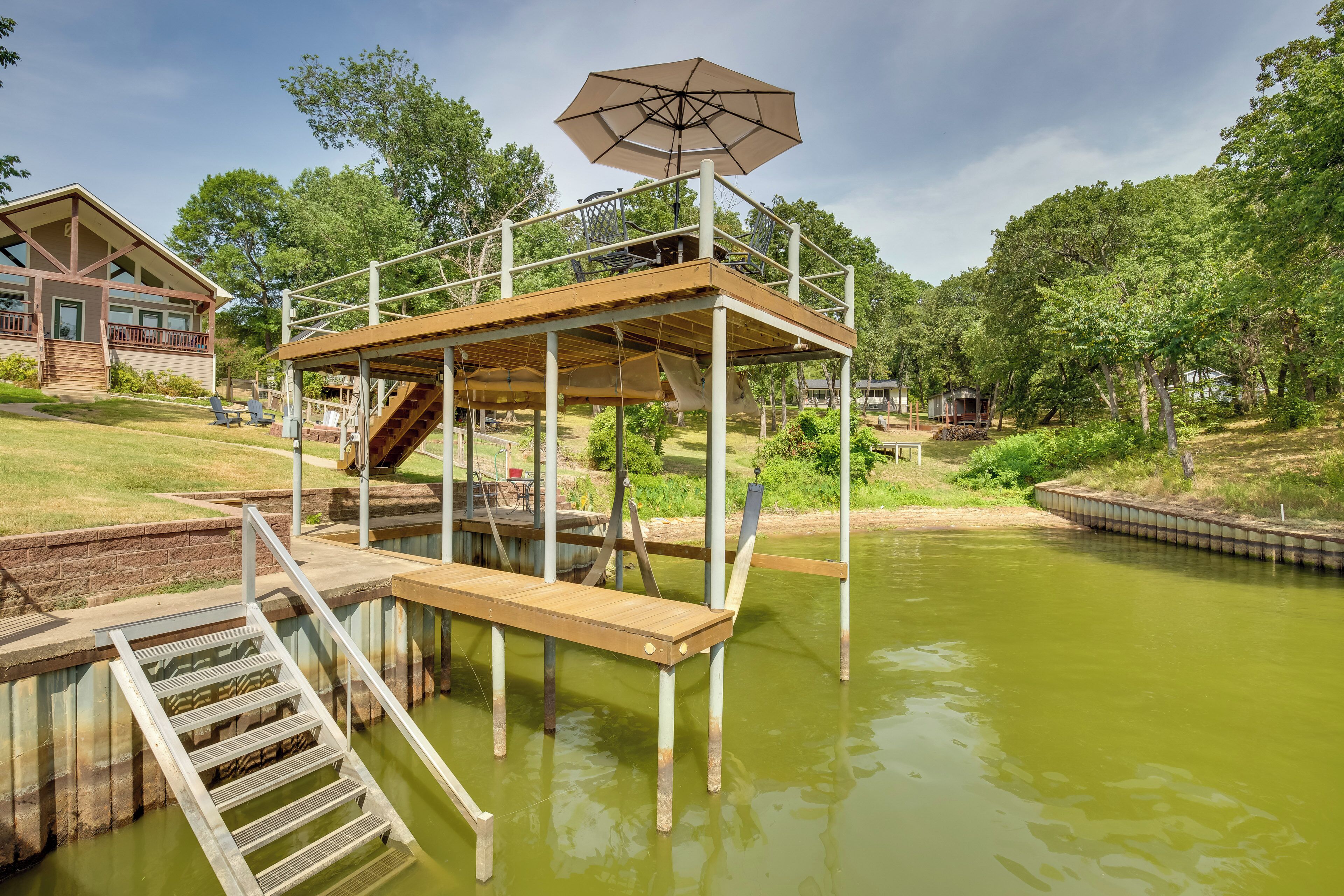 A wooden deck with a metal railing, a covered seating area, and a staircase leading to a higher platform.