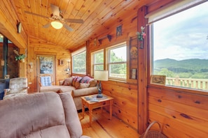 A cozy cabin interior with a wooden ceiling, a ceiling fan, a sofa, a small table, and a window offering a view of the outdoors. - Secluded Mountain Cabin w/ Decks + Gazebo! (Warne)