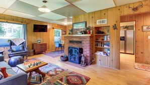 A cozy living room with a fireplace, wooden walls, a television, and a dining area with a chess table. - Peaceful & Scenic Cottage Near Mckenzie River! (Walterville)