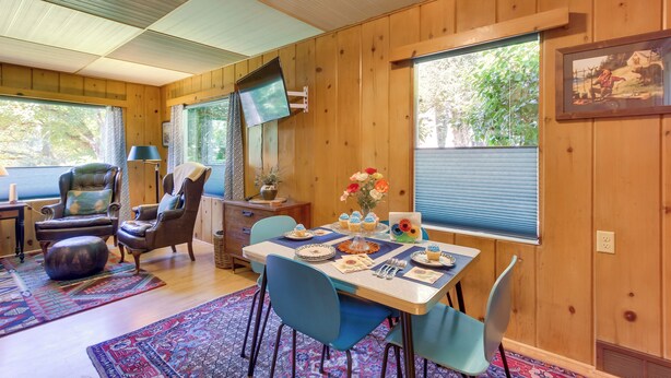 A cozy room with a wooden interior, a dining table set with plates and a vase of flowers, and a television mounted on the wall. - Peaceful & Scenic Cottage Near Mckenzie River! (Walterville)