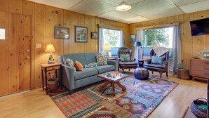 A cozy living room with wooden walls, a blue sofa, a patterned rug, and a chess table. - Peaceful & Scenic Cottage Near Mckenzie River! (Walterville)