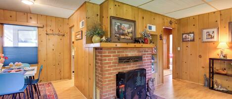 A cozy room with a fireplace, wooden walls, a dining table with chairs, and a rug.