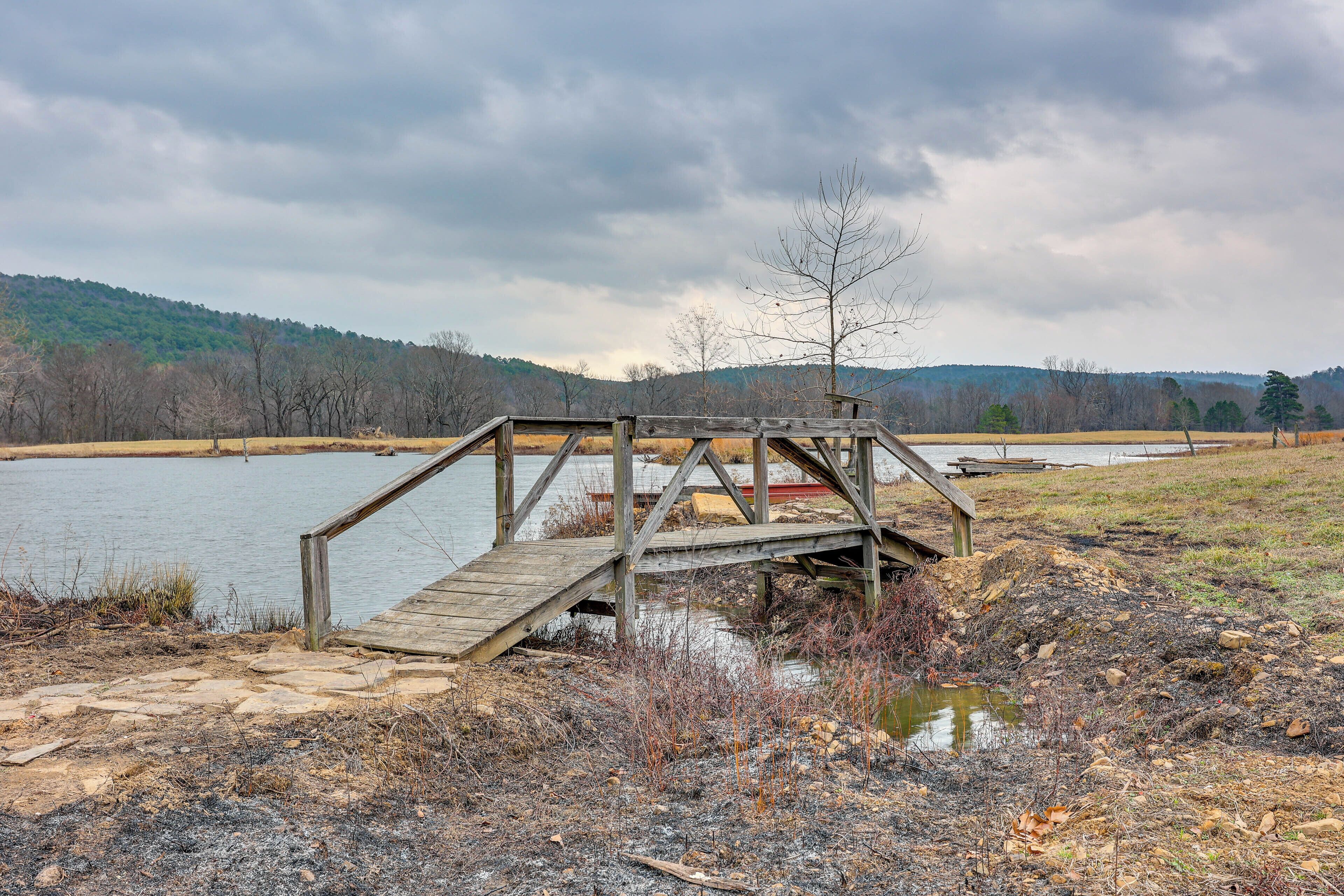A wooden bridge over a body of water with a hilly landscape in the background.