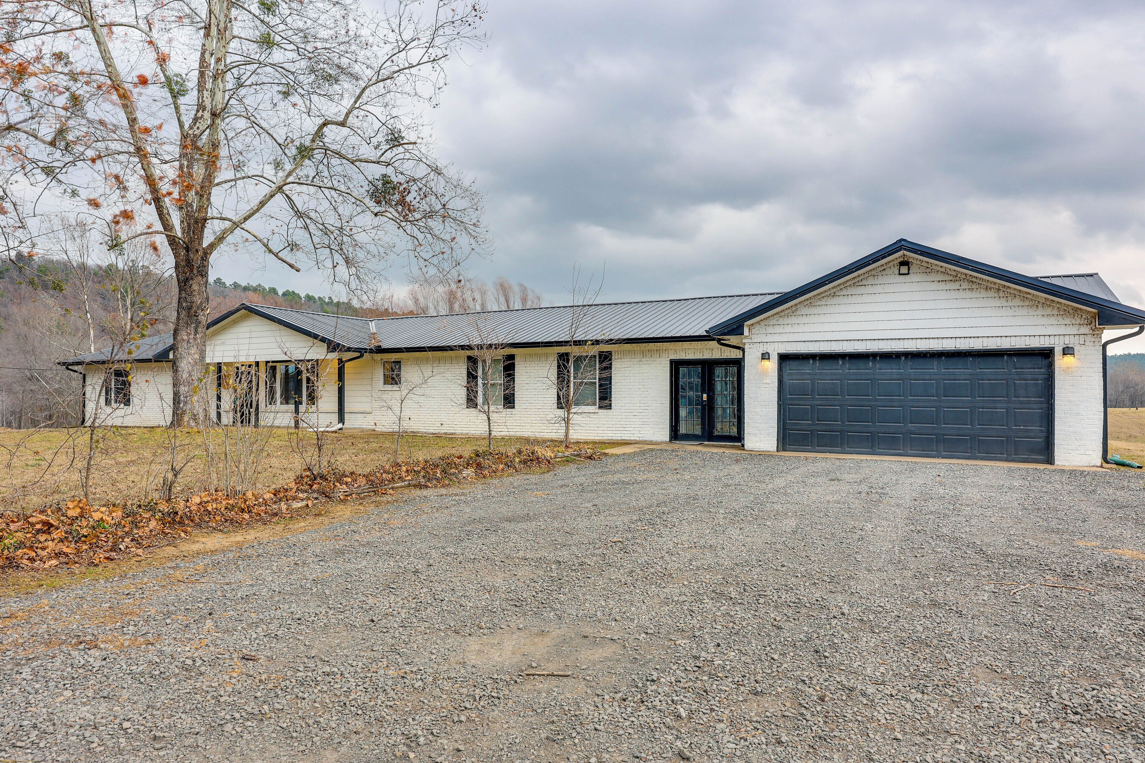 A two-story white building with a garage, surrounded by a gravel driveway and leaf-covered ground.