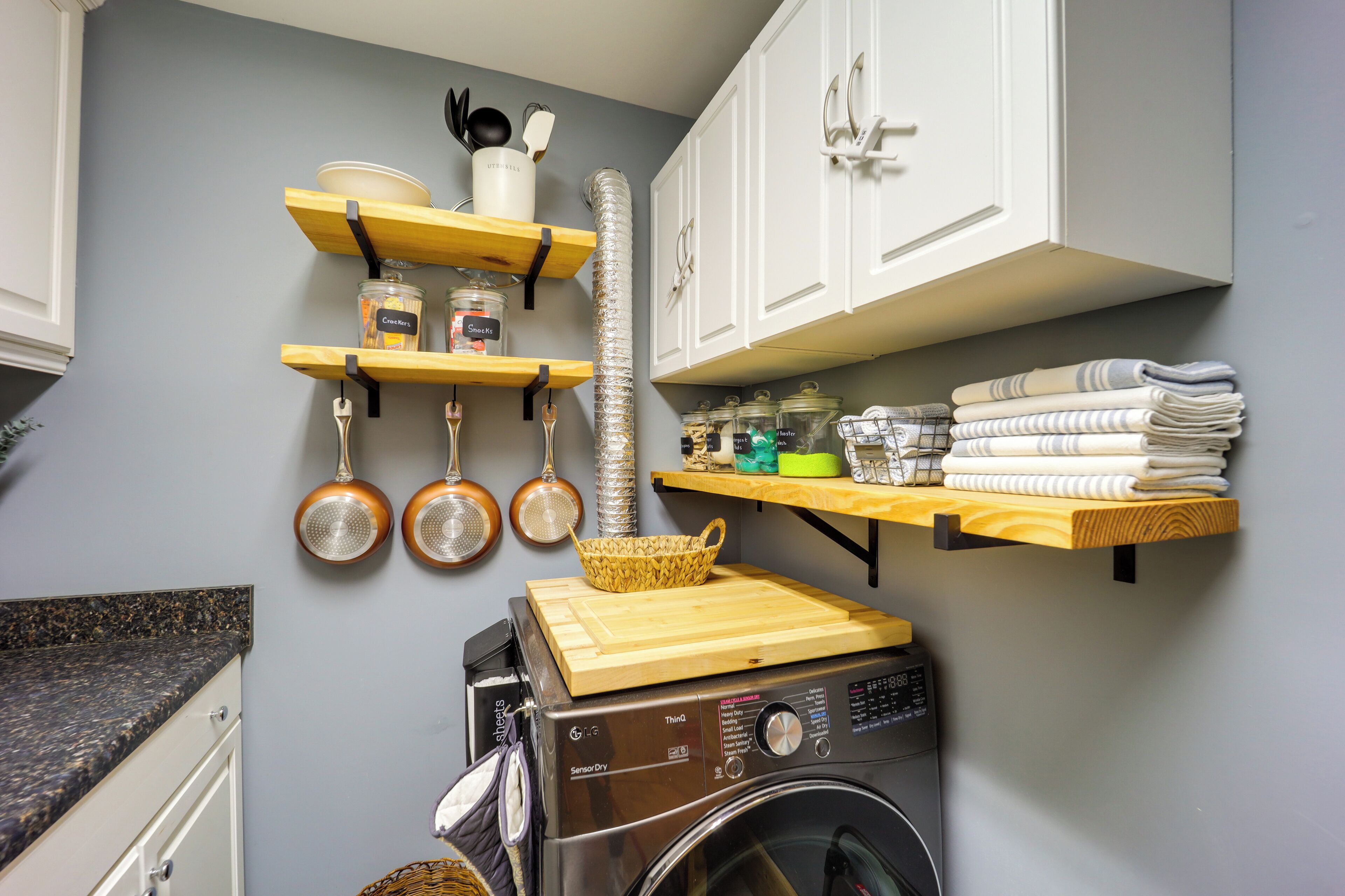 Una cocina con lavadora, repisas de madera con utensilios de cocina y un tendedero.