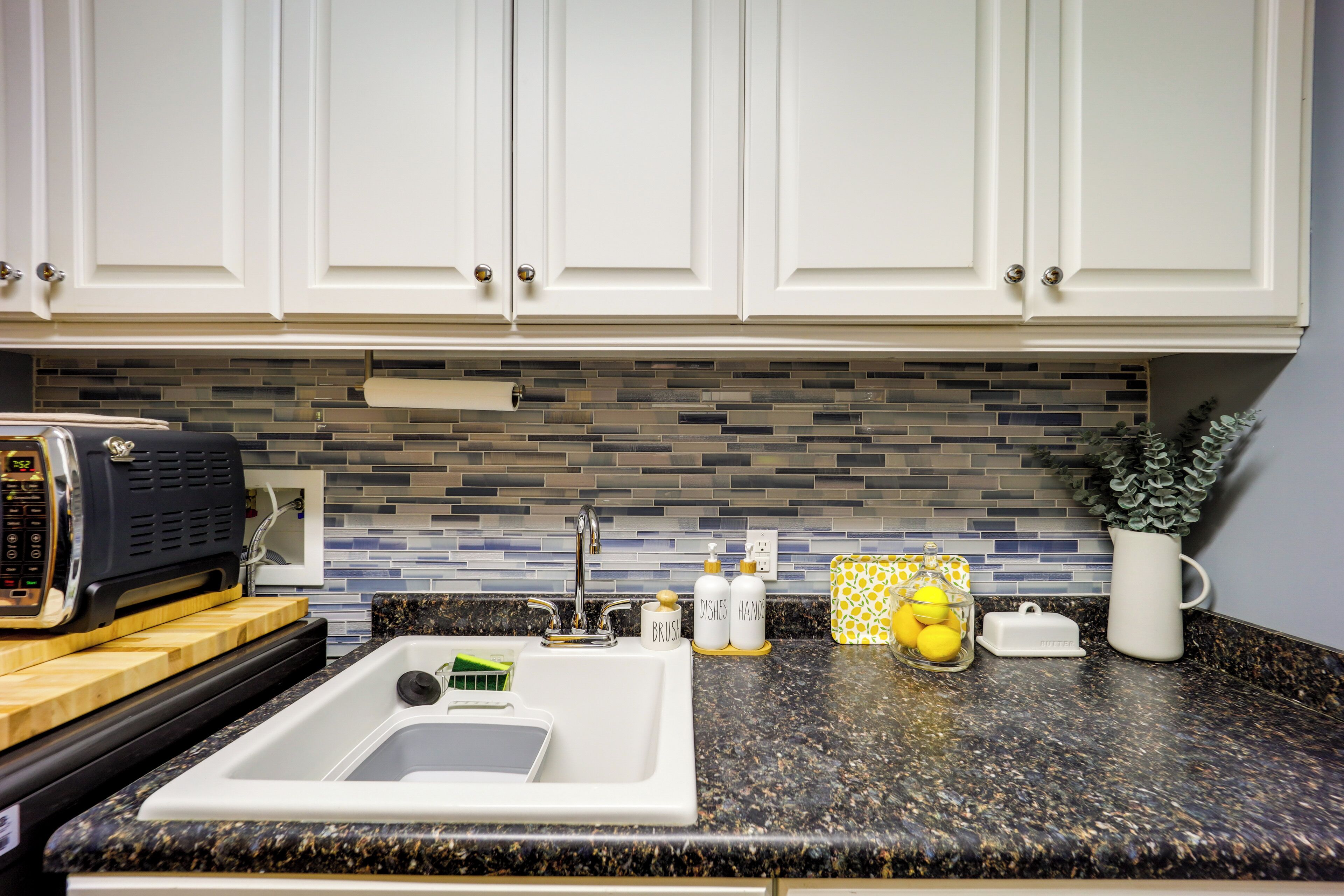 A kitchen with white cabinets, a granite countertop, a toaster, a sink, and a backsplash with blue and gray tiles.