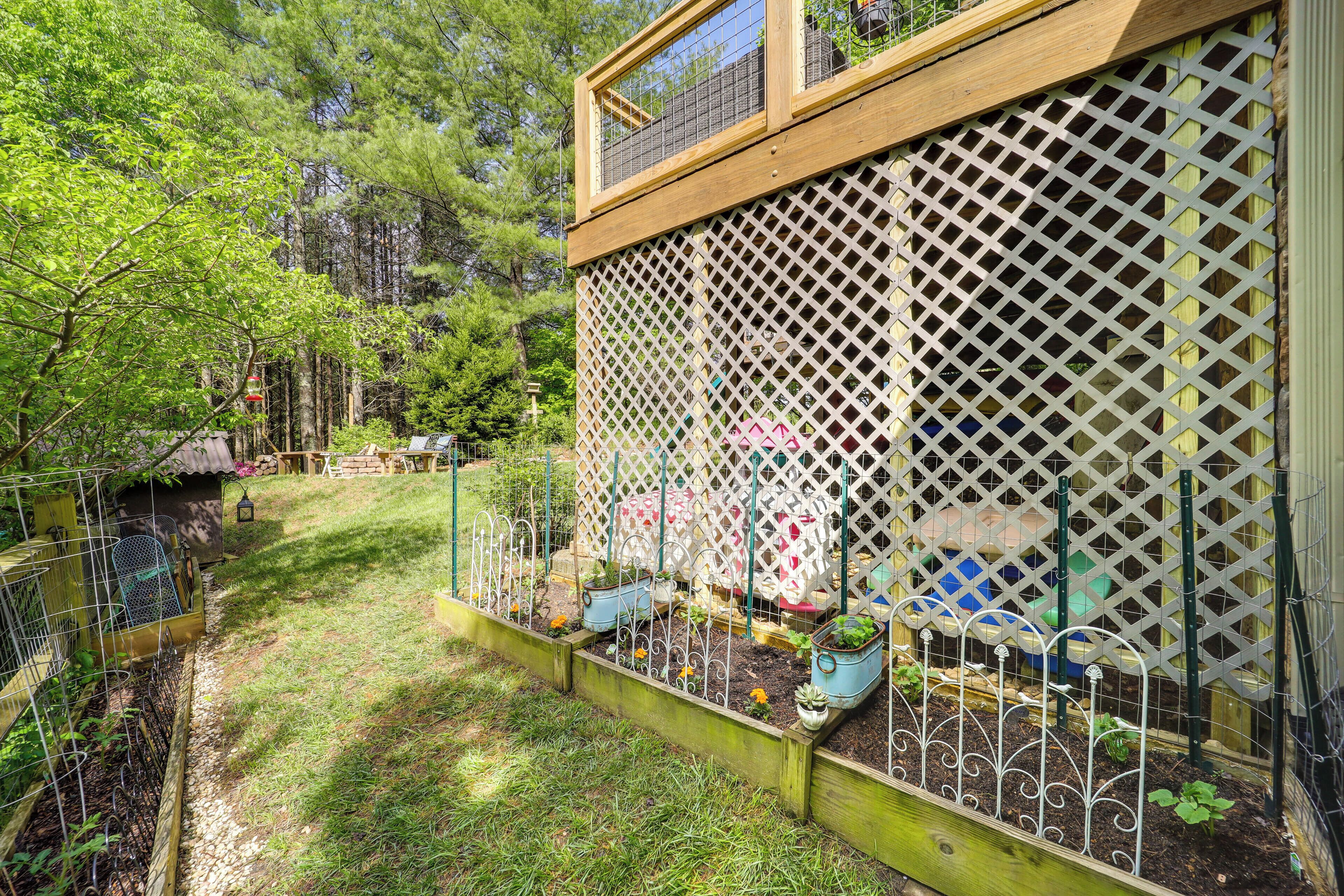 Um jardim com canteiros elevados, um deck de madeira e um cercado treliçado.