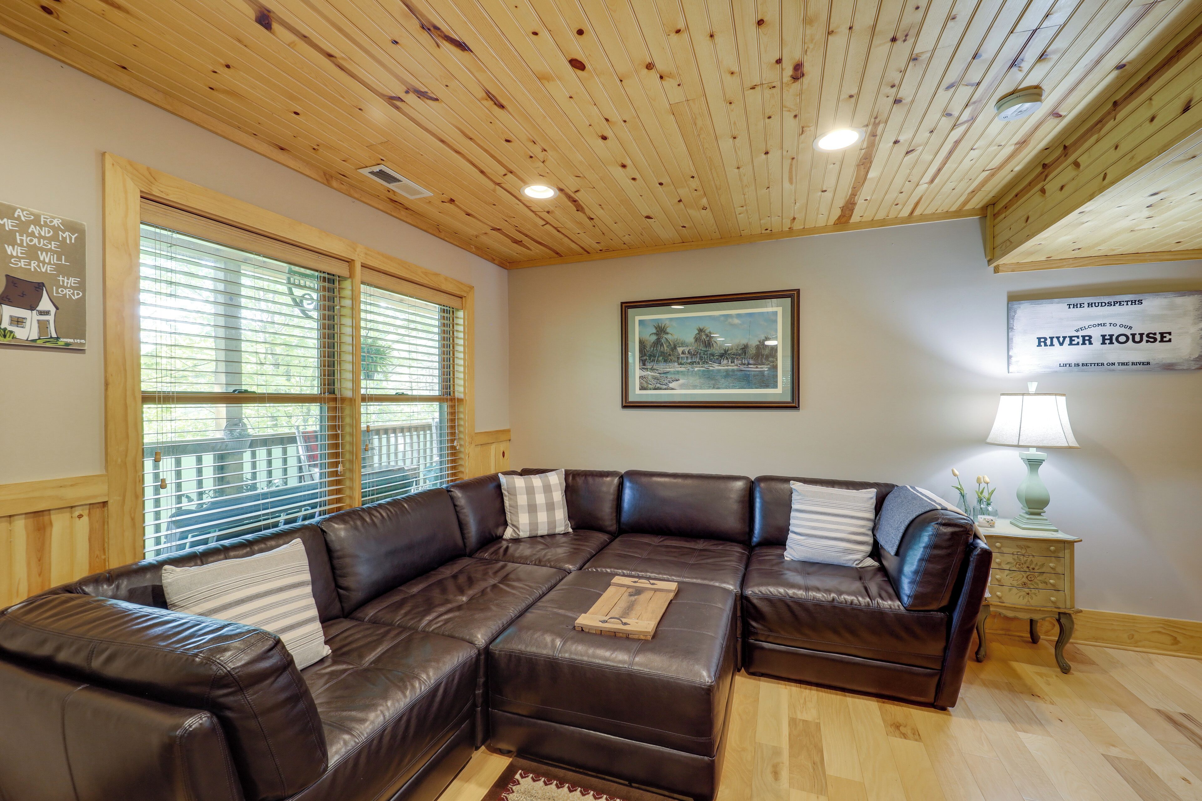 A cozy living room with a sectional sofa, wooden ceiling, and a framed welcome sign.