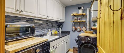 A compact kitchen with white cabinets, a microwave, an oven, a washing machine, and a sink.