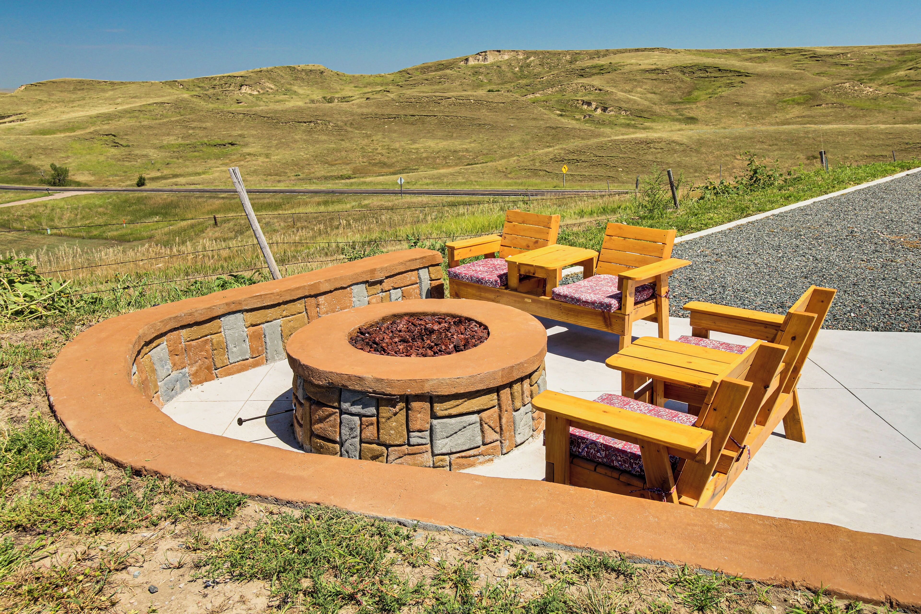 An outdoor patio with a stone fire pit, wooden chairs, and a table.