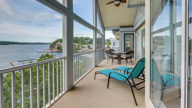 A balcony with a view of a lake, a table with chairs, and a ceiling fan. - Lakefront Ozark Getaway w/ Views + Community Perks (Lake Ozark)