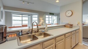 A modern kitchen with a large sink, two windows, a clock, and a view of the lake. - Lakefront Ozark Getaway w/ Views + Community Perks (Lake Ozark)