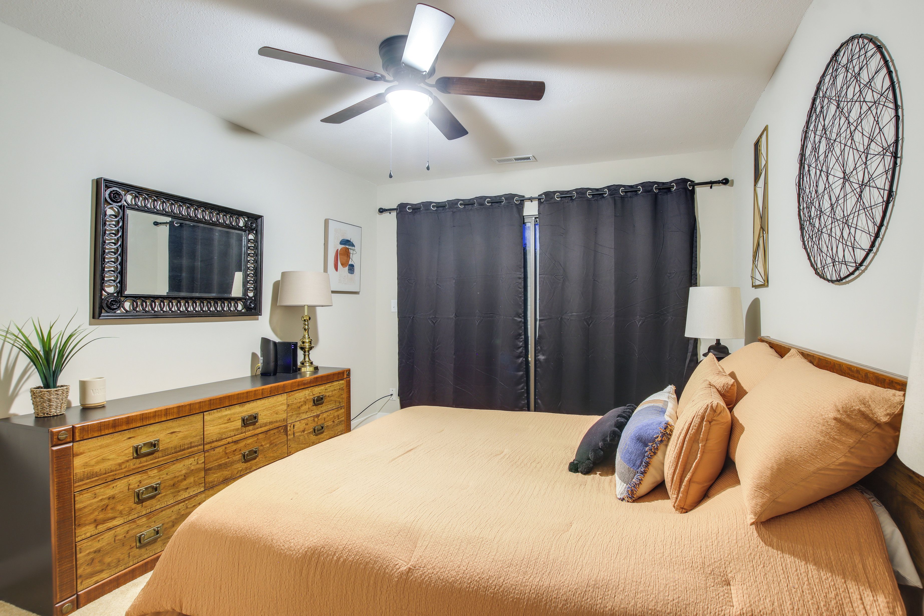 A bedroom with a bed, a dresser, a ceiling fan, a mirror, and curtains.