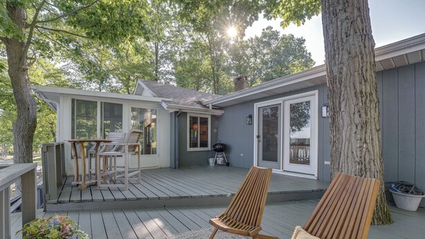 A wooden deck with a chair and a table, a potted plant, and a large tree. - Delton Oasis Retreat w/ Lake Views & Deck! (Delton)