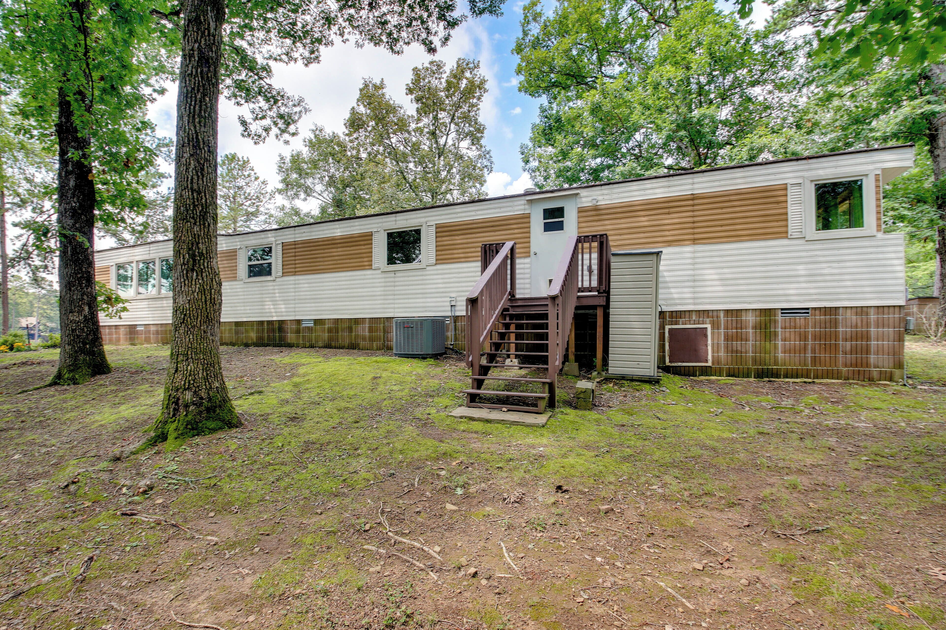 A mobile home with a wooden exterior, a staircase leading to the entrance, and a fenced yard with trees.