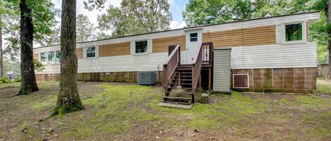 A mobile home with a wooden exterior, a staircase leading to the entrance, and a fenced yard with trees.