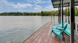 Une jetée en bois, dotée de chaises et d’un espace abrité, offre une vue sur un lac paisible dont les rives sont bordées d’une forêt.