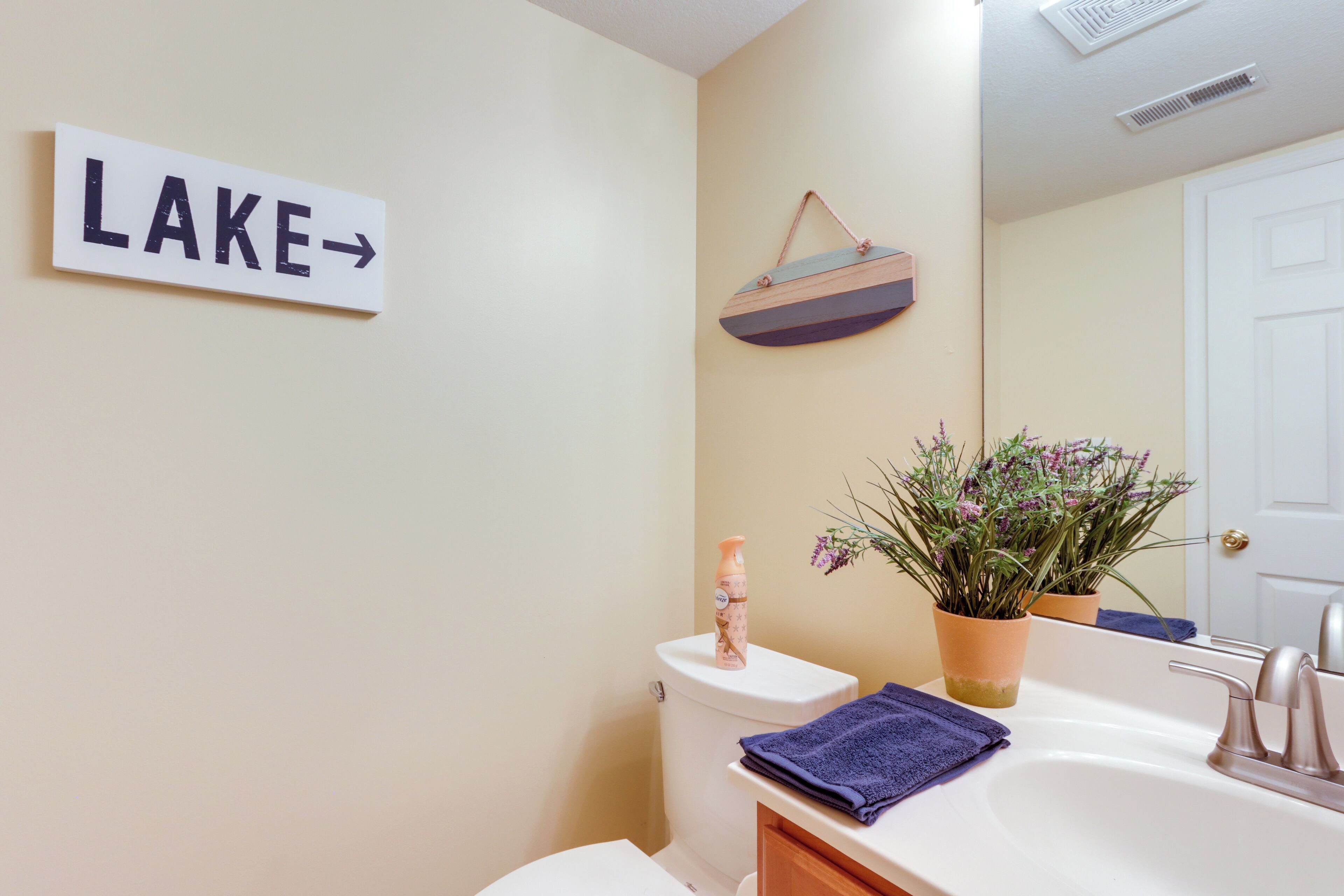 Ein Badezimmer mit Toilette, Waschbecken, Spiegel und einem Schild mit der Aufschrift 'LAKE' und einem Pfeil.