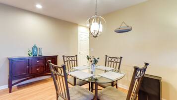 A dining area with a glass table, four chairs, a chandelier, a dark wooden cabinet, and a small refrigerator.