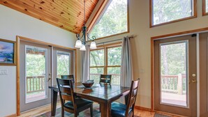 A dining area with a wooden table, four chairs, and a chandelier. There are large windows with curtains, a wooden ceiling, and a view of trees outside. - Marble Mountainside Escape w/ Wraparound Deck (Marble)