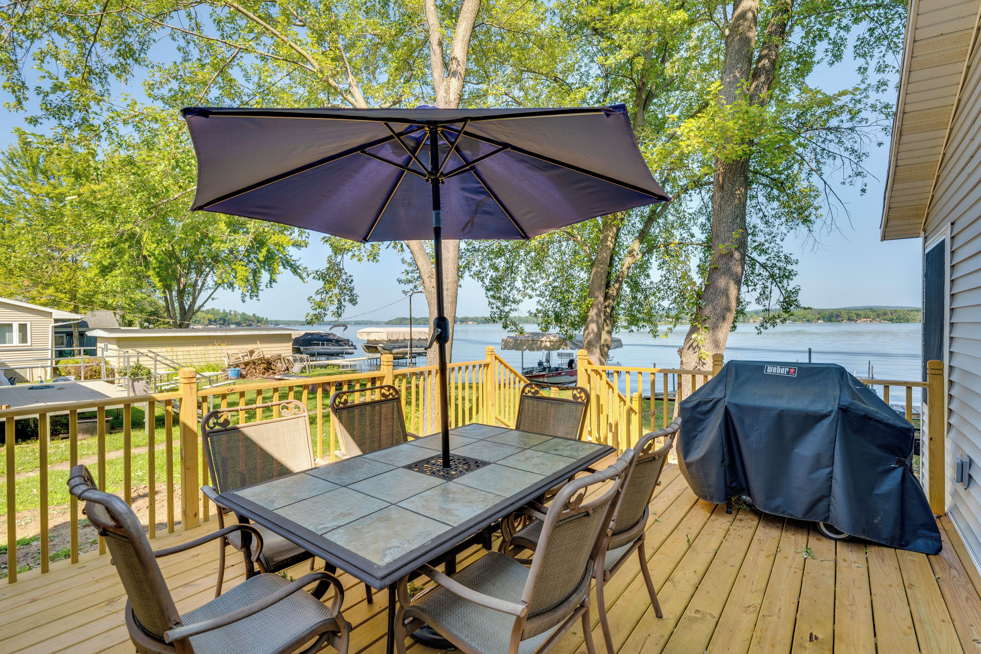Un terrazzo in legno con tavolo e sedie, un barbecue e vista sul lago.