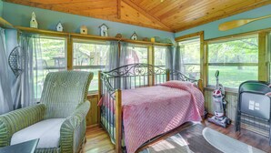 A cozy room with a wooden ceiling, a bed with a pink quilt, a wicker chair, and a window with curtains. - Riverfront Nature Getaway Near Downtown Pine City! (Pine City)